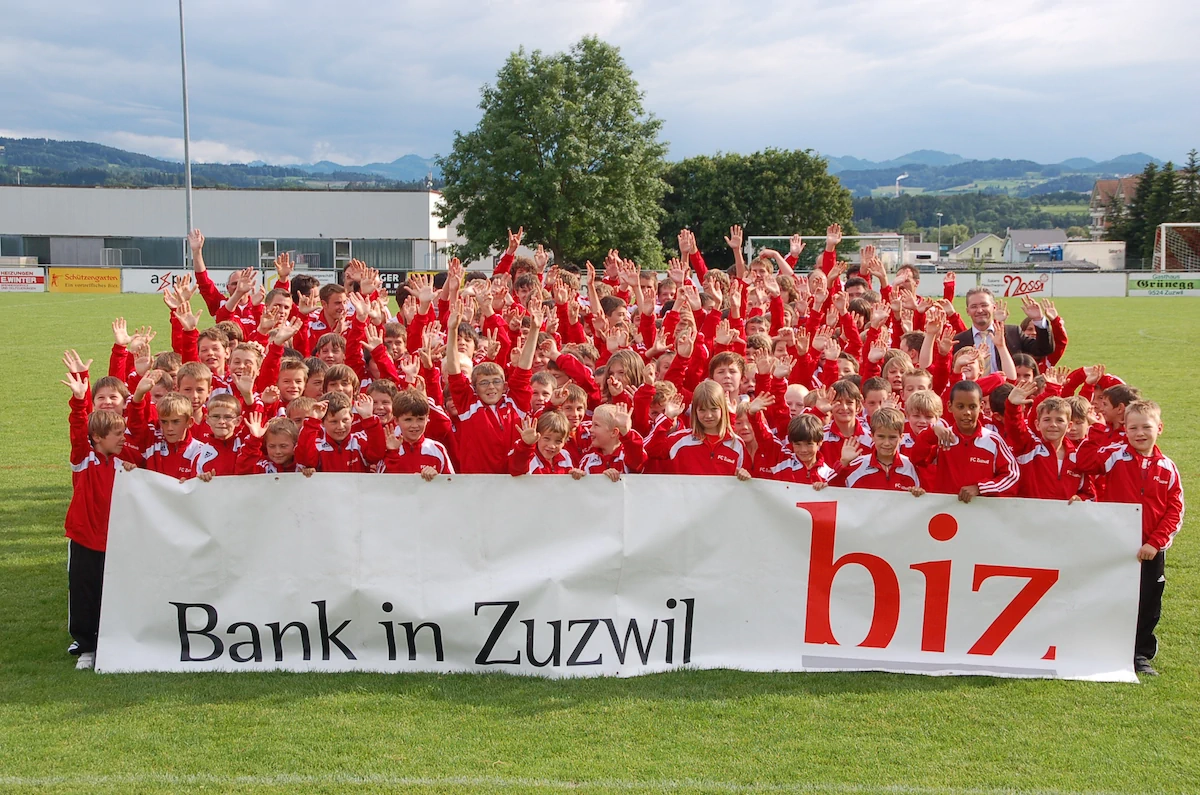 Gruppenbild des FC Zuzwil mit roten Trainerjacken und grossem BIZ Banner